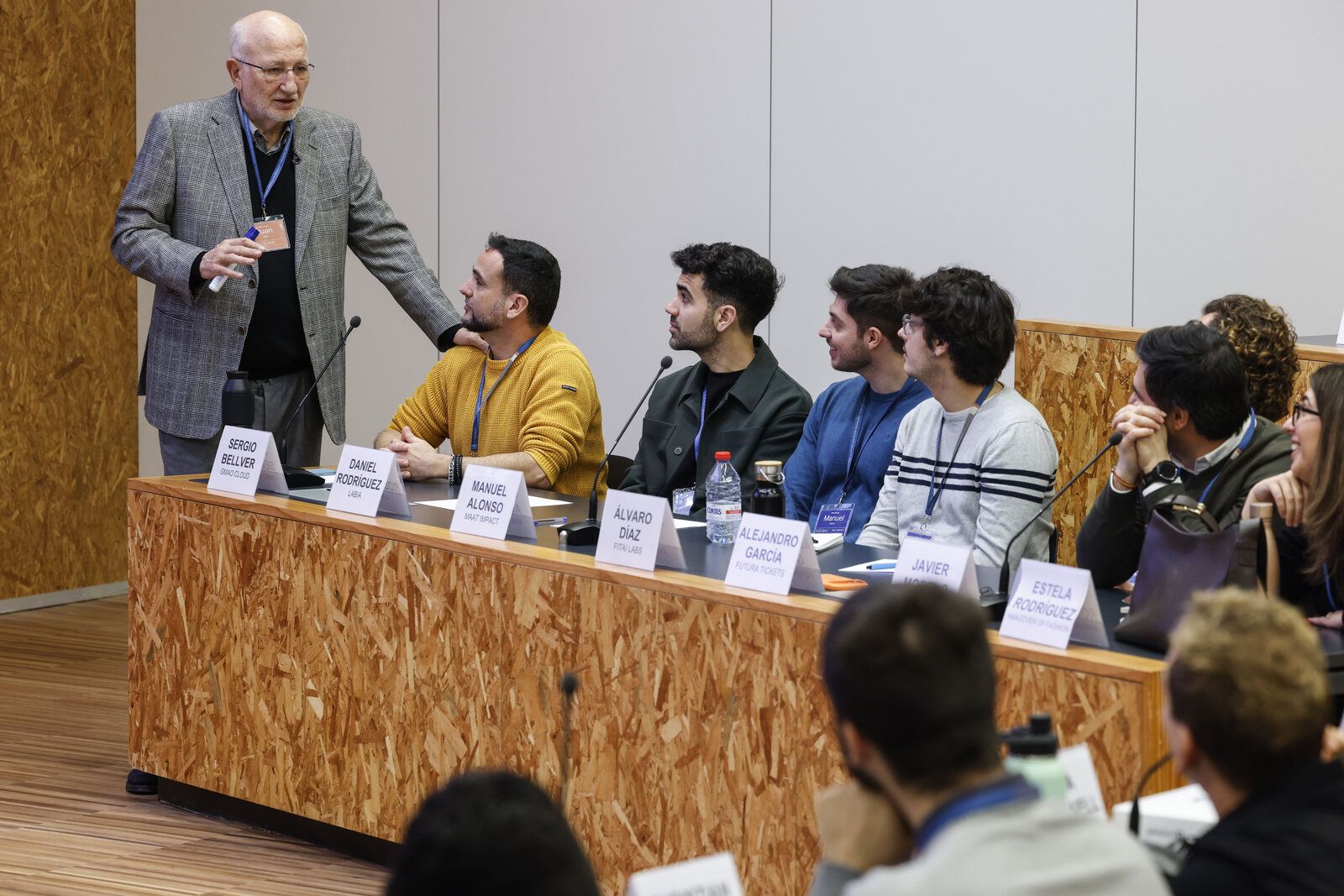 Sergio Bellver, de GMAO CLOUD, sentado en la mesa de ponentes de la jornada de cierre del programa Calidad Total de Lanzadera, con Juan Roig de pie a su lado dirigiéndose a los participantes.